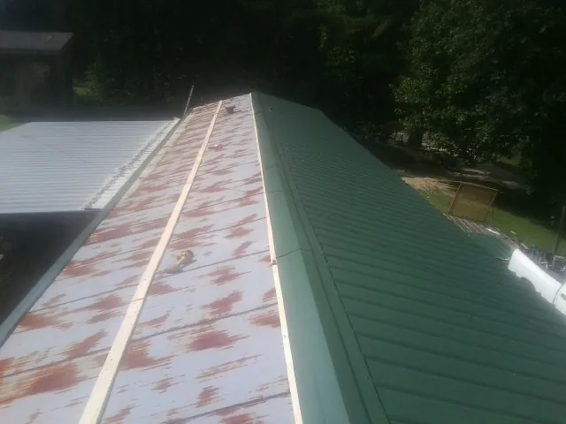 Old rusted panels beside newly installed green metal roofing — Wind Damage Roof Repair by Roofing Brothers in Caryville