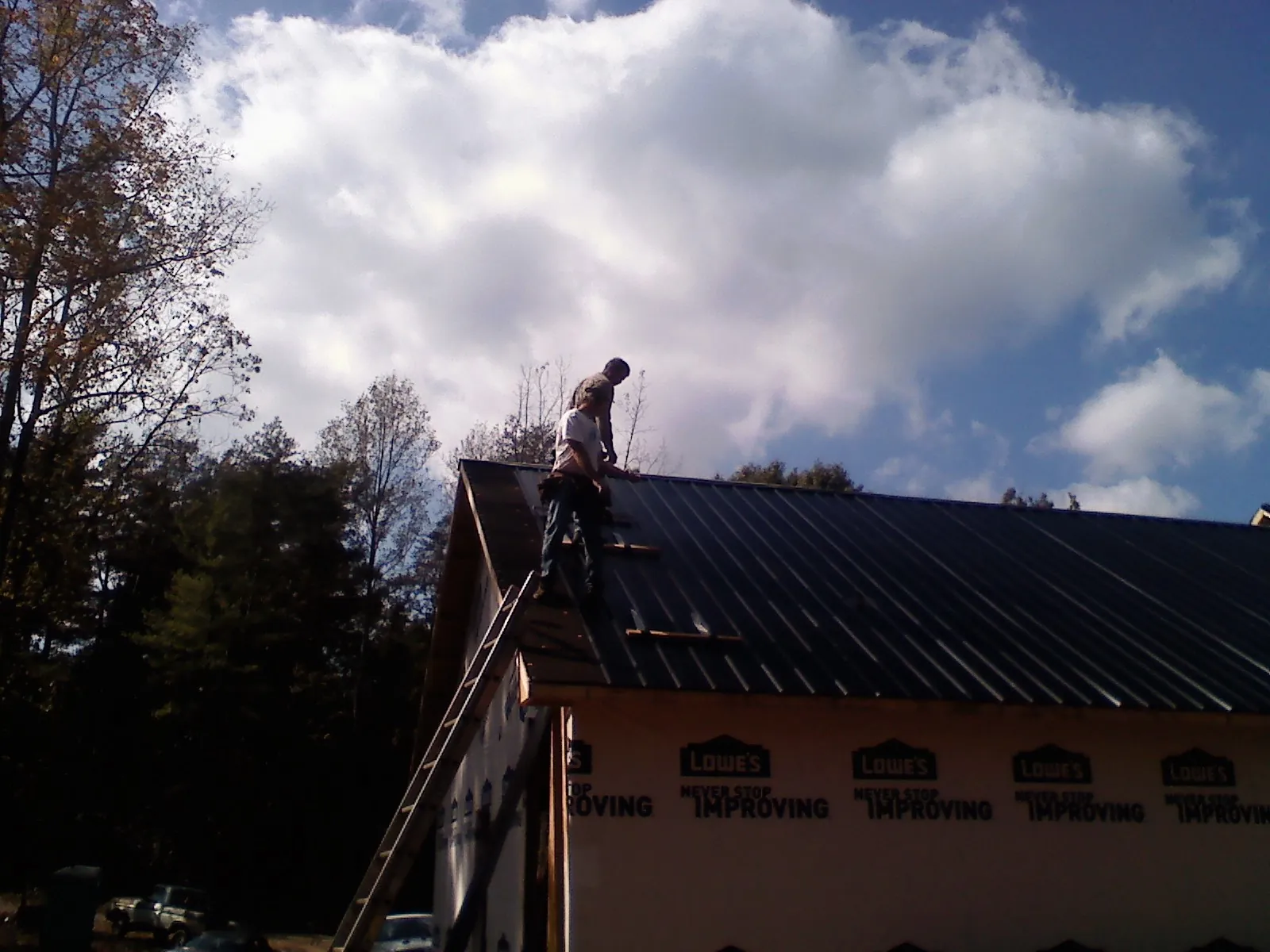 Roofer fastening dark metal panels high against a cloudy sky, from a Roof Inspection job in Caryville