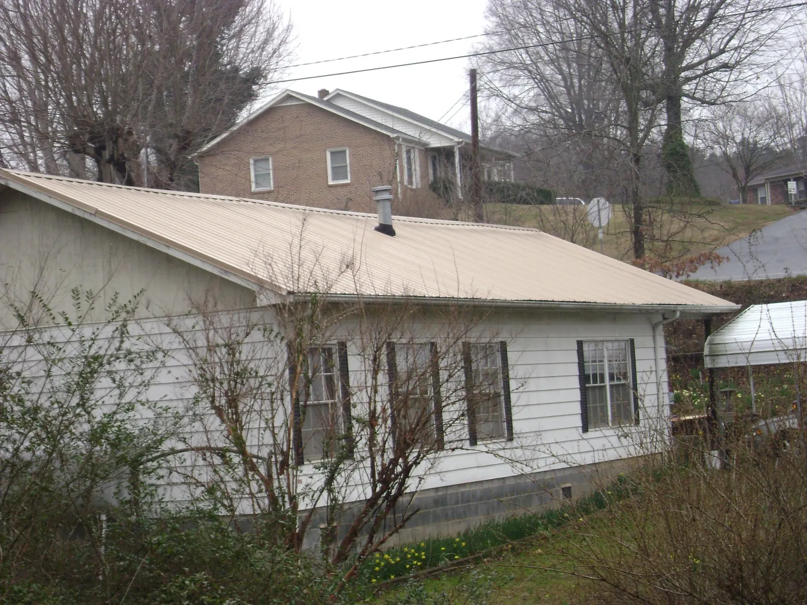 Tan metal roof on a white sided house set into a hillside — Commercial Roofing by Roofing Brothers in Caryville